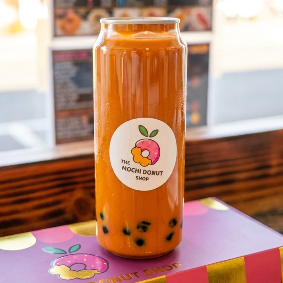 A Mochi Donut Shop bubble tea in a can and a purple box on a wooden counter.